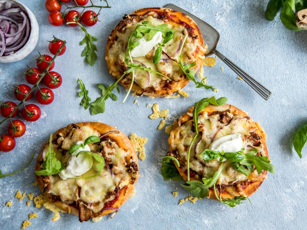 Tre vegetariske pitapizzaer med ost, grønnsaker og salat på toppen, ser ut til å være på en tallerken eller et fat.