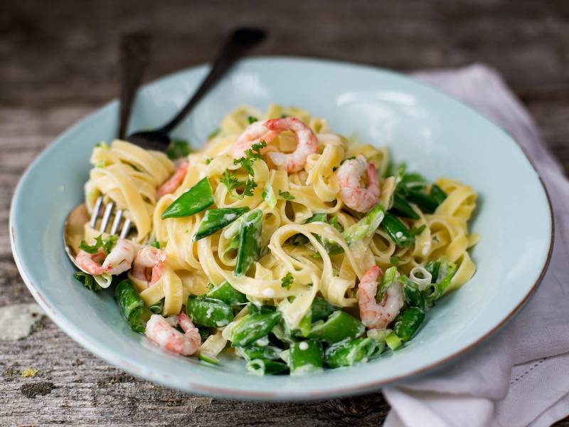 Pasta med reker og grønnsaker på en hvit tallerken, servert med en gaffel og skje på siden.
