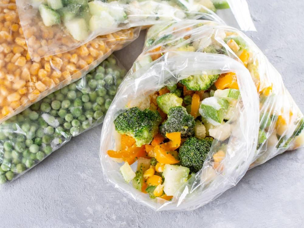 Frosne grønnsaker i plastposer, inkludert brokkoli, gulrot og erter.