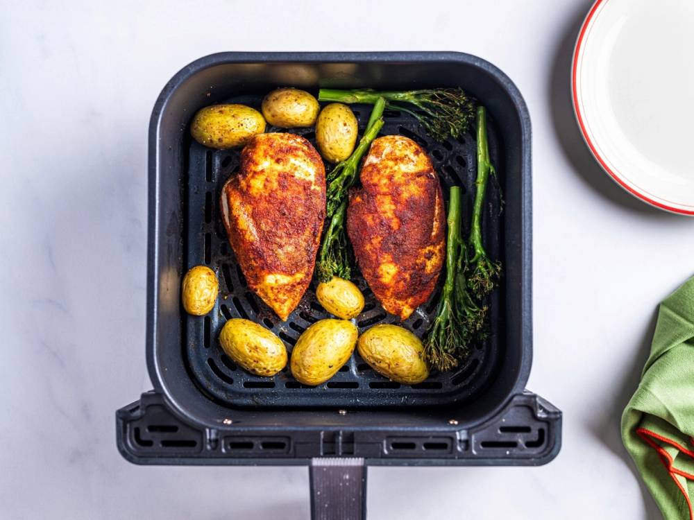 Kyllingbryst og små poteter stekes i en airfryer med grønne grønnsaker ved siden av