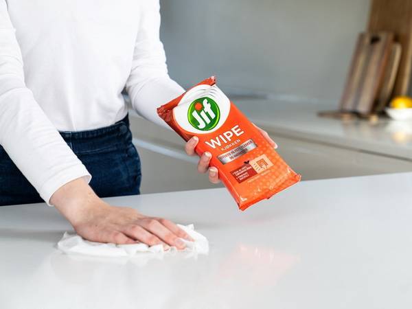 Person som tørker av kjøkkenbenken med Jif Wipes, med kjøkken i bakgrunnen.
