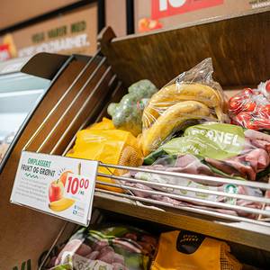 Omplassering av frukt og grønt i en butikk, med en skilt som viser pris på 10 kroner for eple og annen frukt.