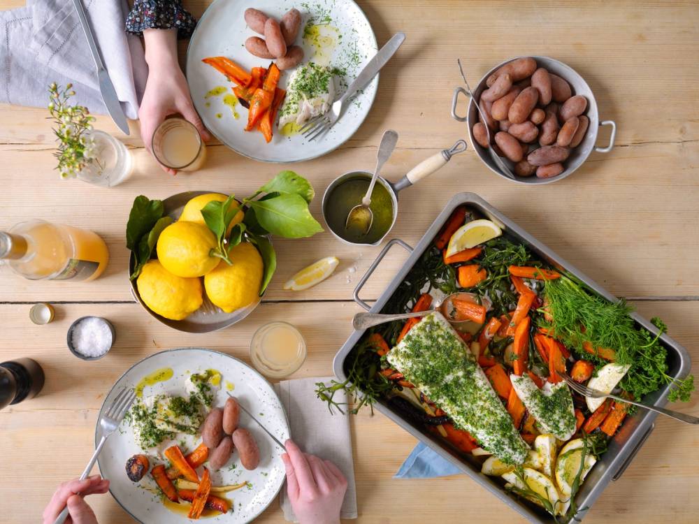 Personer som spiser og deler fiskeretter på et bord med grønnsaker og sitroner under en fiskefest.