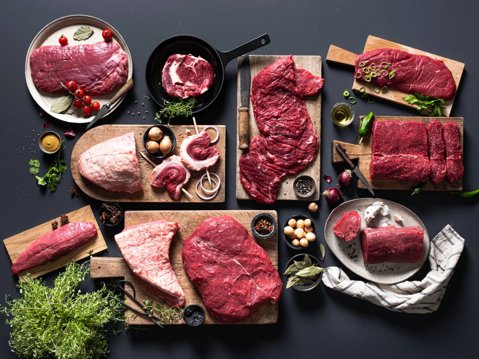 Ulike typer av rått kjøtt, inkludert biffer og steker, er lagt ut på skjærebrett og tallerkener på et kjøkkenbord.