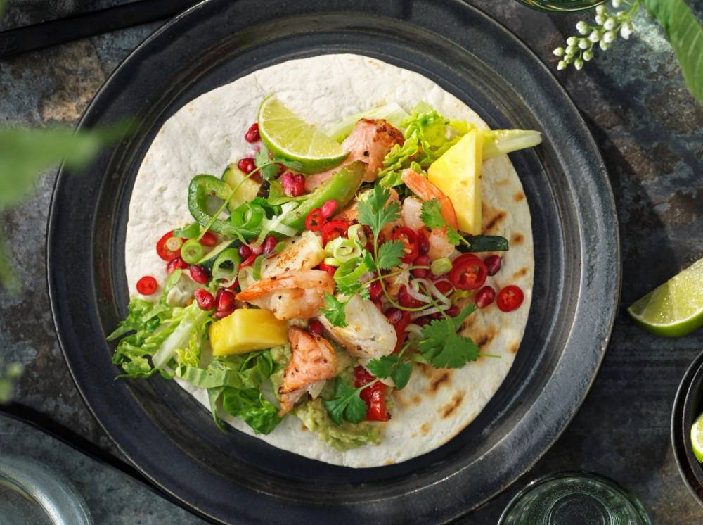 Fiskewok i tortilla med grønnsaker og limebåter på en svart tallerken