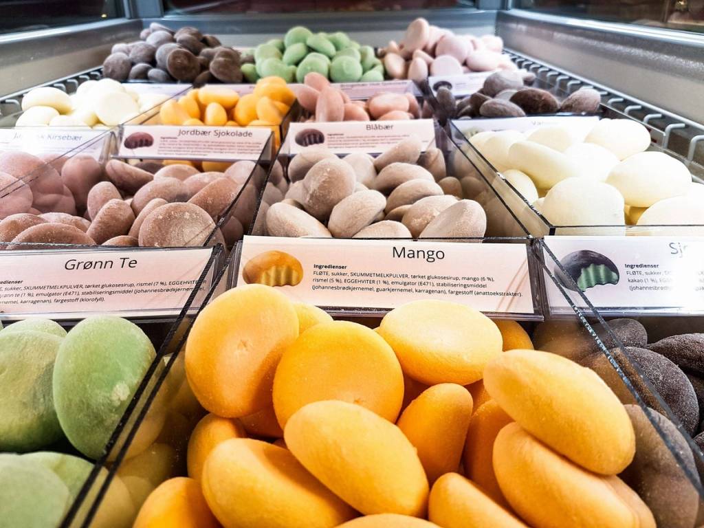 Fargerike og ulike typer boller i en butikkdisk, med etiketter som viser smaker som grann te og mango.