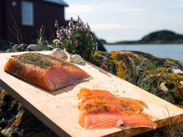 Røkt laks på et skjærebrett med blomster og sjø i bakgrunnen på Espevær.