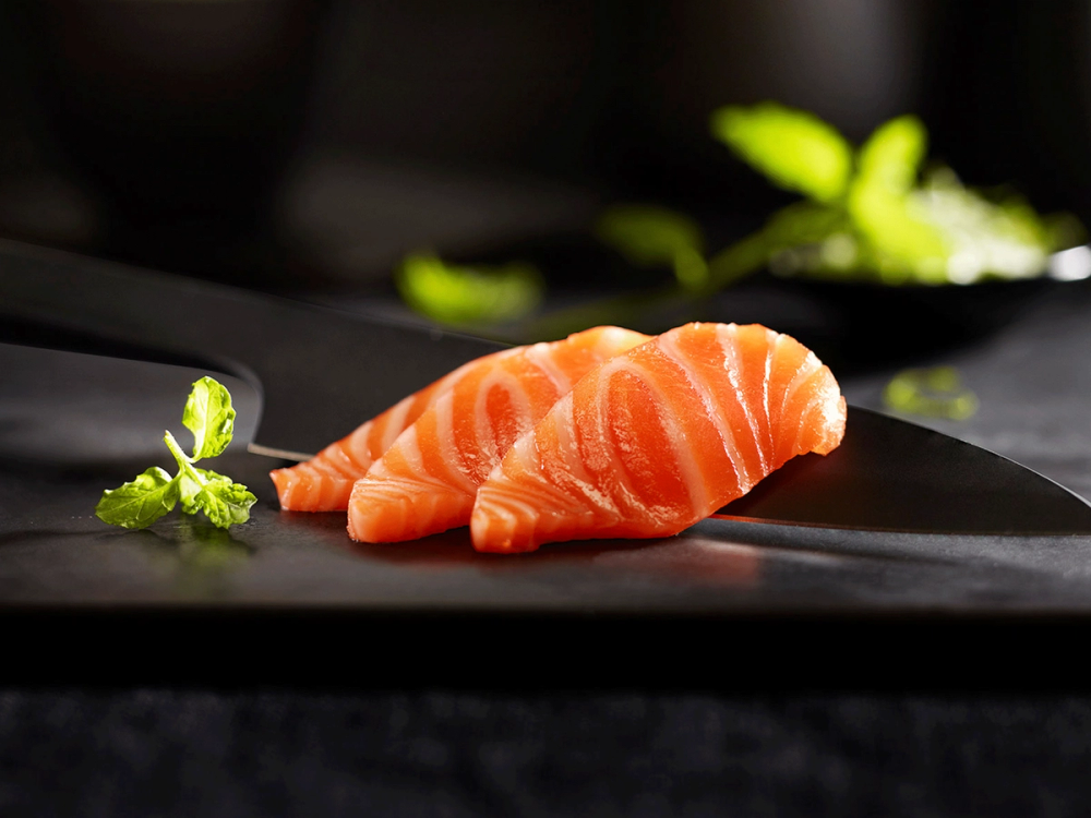 To laksefileter på en svart tallerken med grønne urter ved siden av.