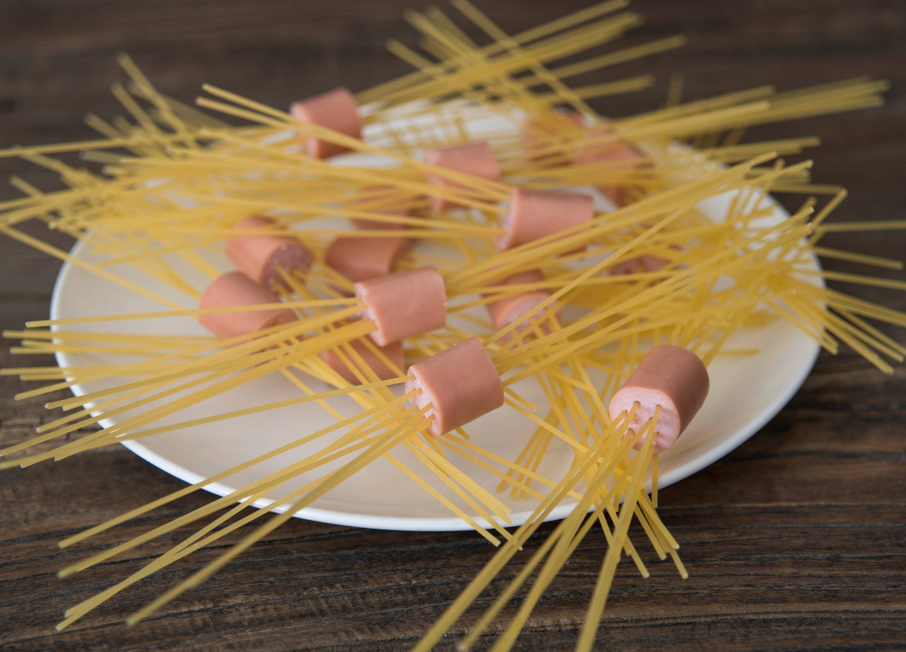 Spyd av spaghetti med kjøttboller på en hvit tallerken, satt på et trebord.