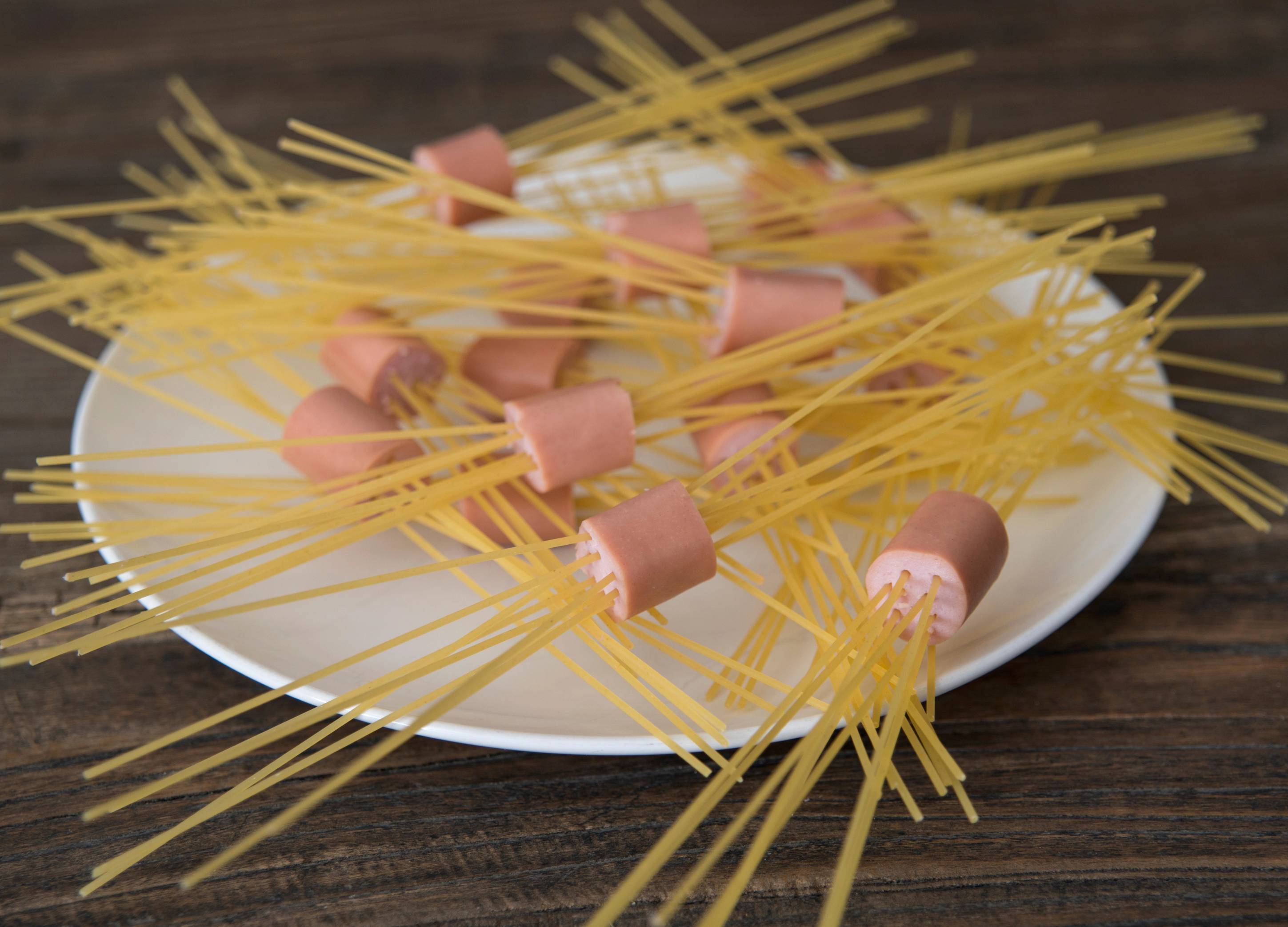 Spyd av spaghetti med kjøttboller på en hvit tallerken, satt på et trebord.