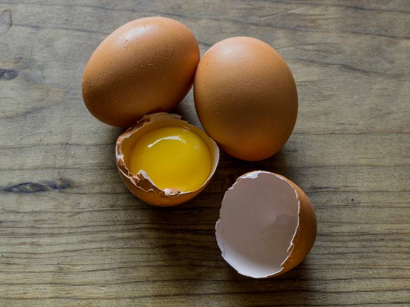 To hele egg og ett knust egg med rått egg inni på en treplate.