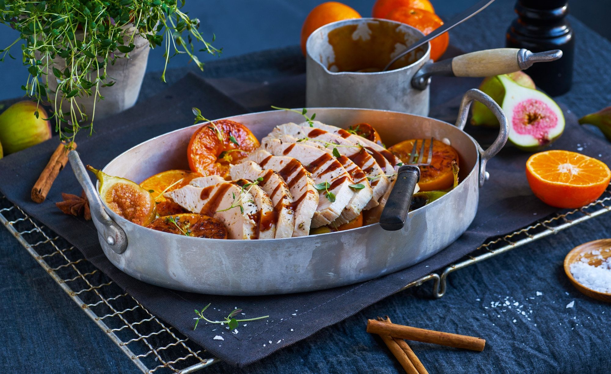 Kalkunbryst skåret opp og servert med sitronbåter i en stor metallform, omgitt av urter og krydder på et mørkt bord.