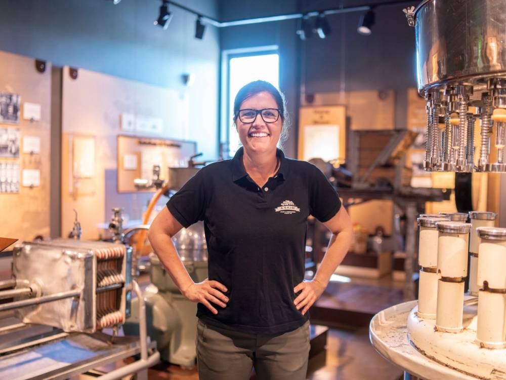 En person står med hendene på hoftene i en industriell eller laboratorie-lignende setting, med utstyr og maskiner rundt seg.