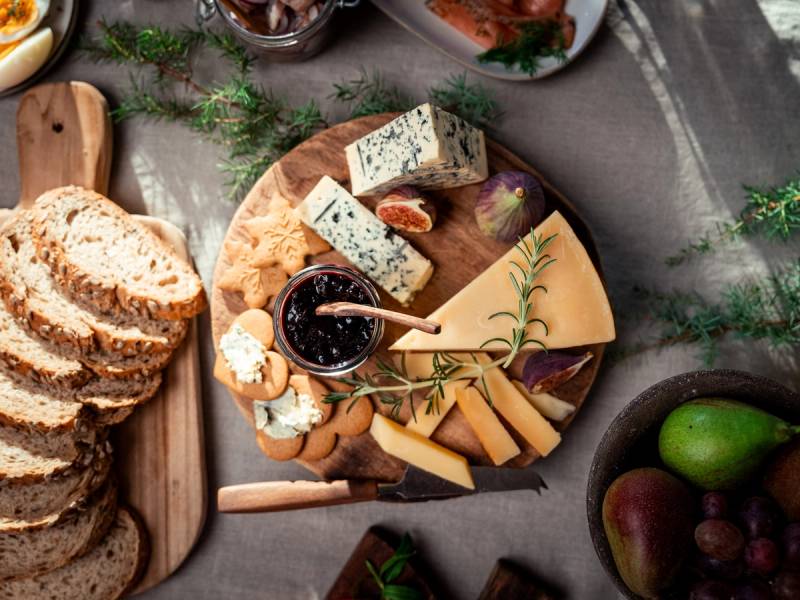 Et utvalg av oster, kjeks og druer på et serveringsfat med grønne urter rundt, sett fra oven.