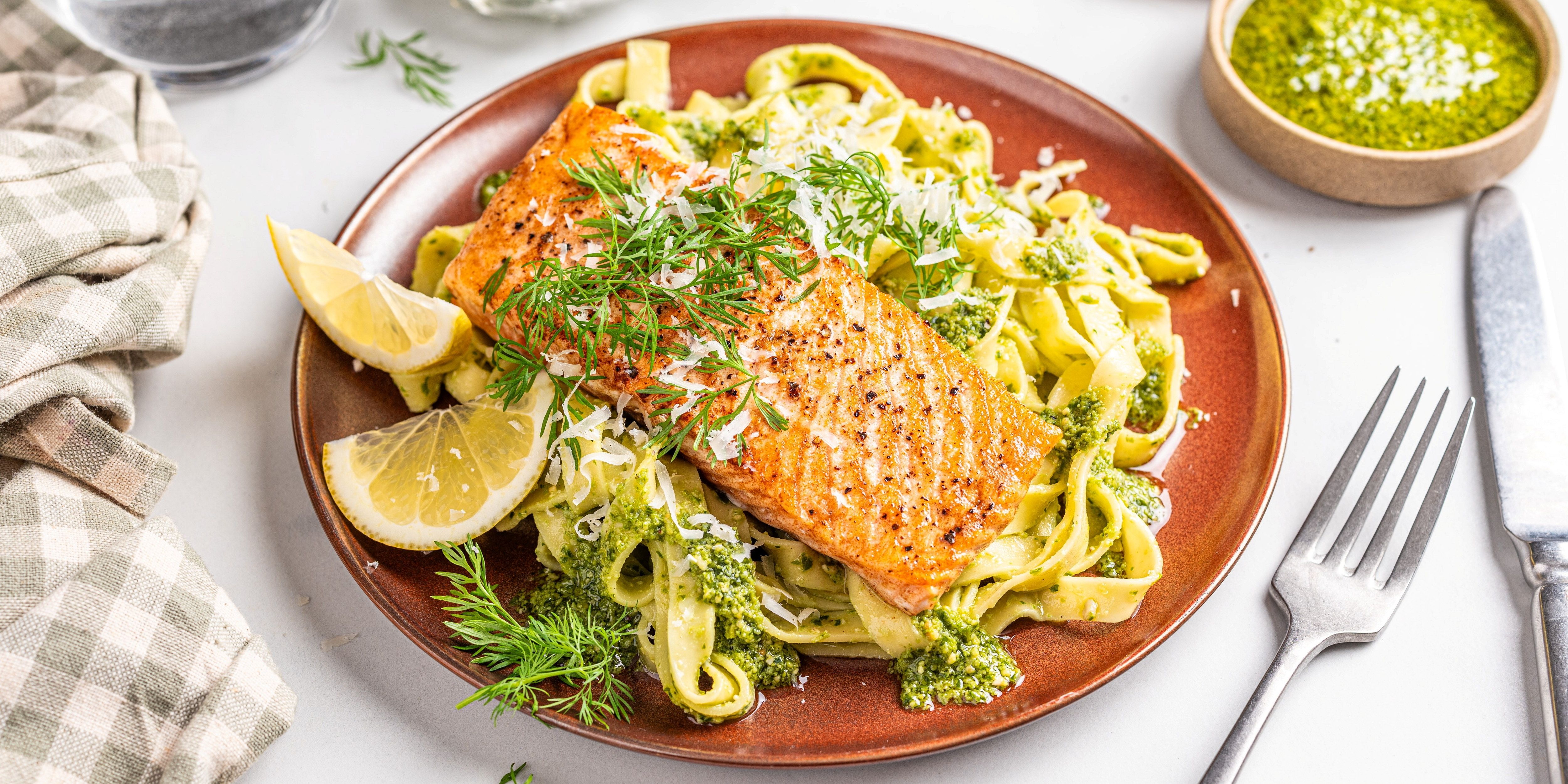 Laks med tagliatelle og pesto på en tallerken, pyntet med sitronbåter og fersk dill