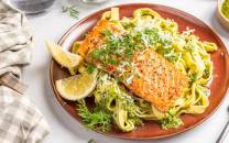 Laks med tagliatelle og pesto på en tallerken, pyntet med sitronbåter og fersk dill