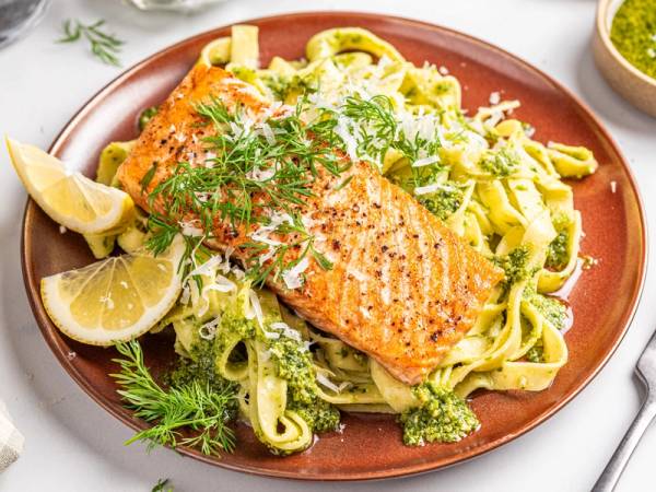 Laks med tagliatelle og pesto på en tallerken, pyntet med sitronbåter og fersk dill