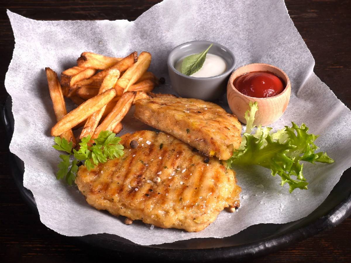 Friterte kyllingfileter med pommes frites og to typer saus, servert på et svart fat med grønne urter som pynt.