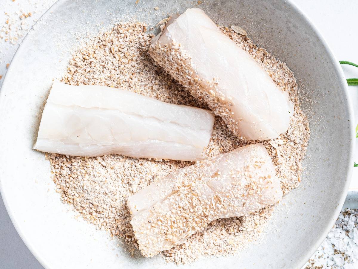 Tre stykker fisk som blir panert i en skål med brødsmuler