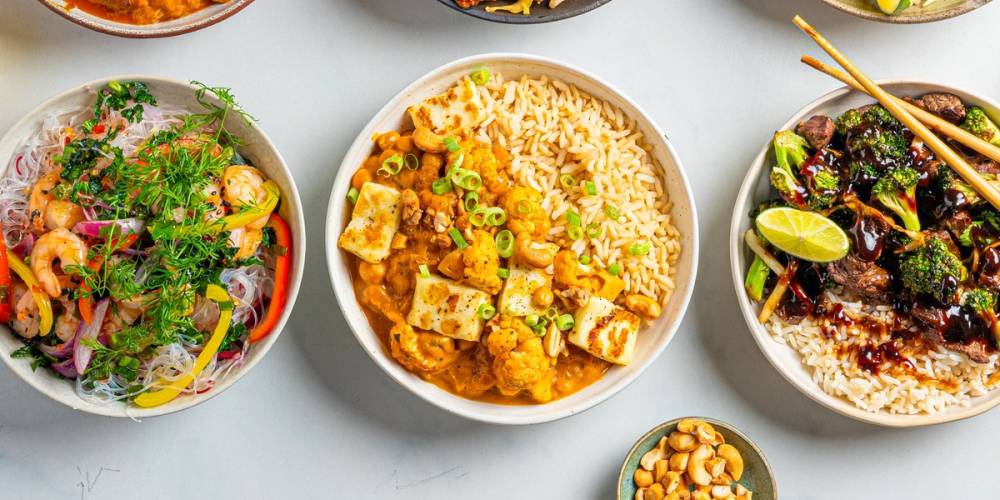 Tre asiatiske retter i boller med ris, grønnsaker og kjøtt, servert på et bord.