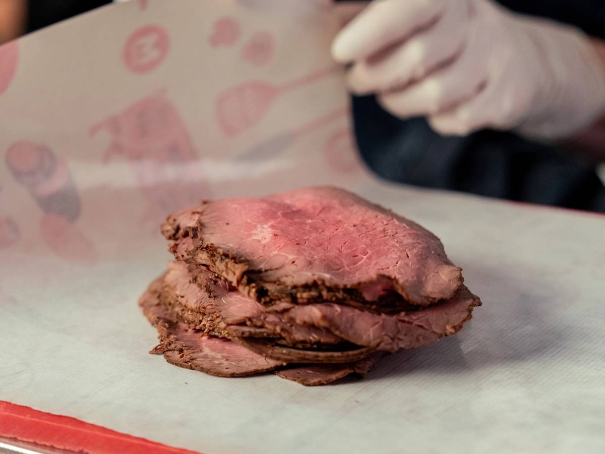 Skiver av roastbiff ligger på et papir med en person i bakgrunnen som holder en kniv.