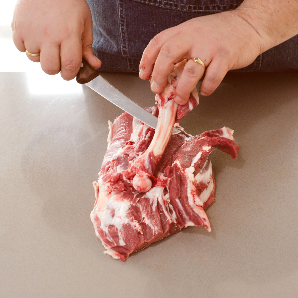 Person som skjærer i et stykke kjøtt med bein på en kjøkkenbenk