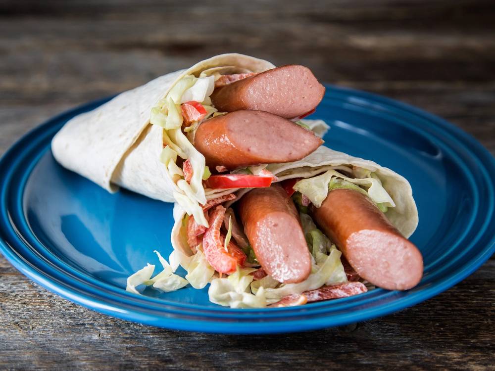 Pølsewrap med pølser, salat og tomat i en tortilla på en blå tallerken.