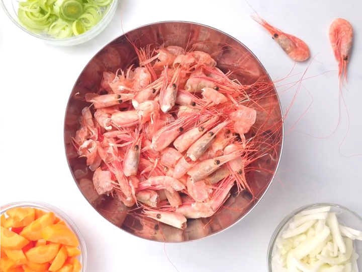 Rekeskallkraft i en bolle med ferske reker rundt på et hvitt bord