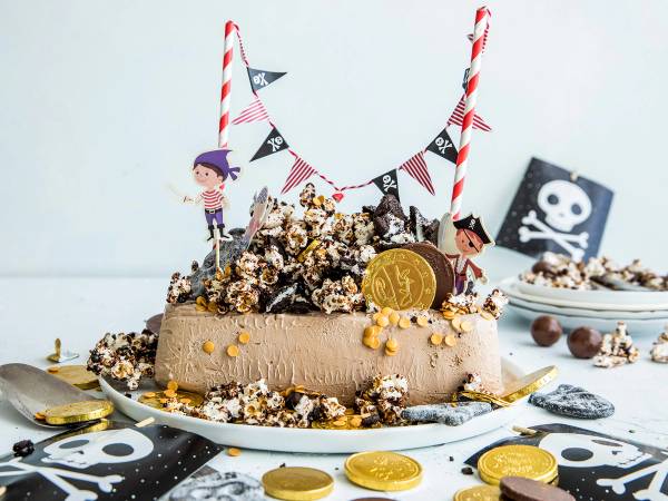 Sjokoladekake dekorert med sjørøvertema, inkludert piratflagg, små piratfigurer, gullmynter og sjørøverskatter, med en hvit bakgrunn.