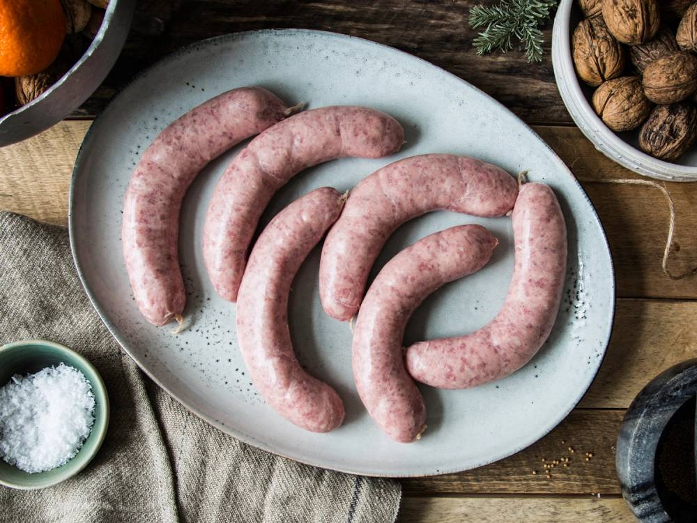 Fire rå julepølser på en hvit tallerken med krydder og nøtter rundt, på et tre- eller trebord.