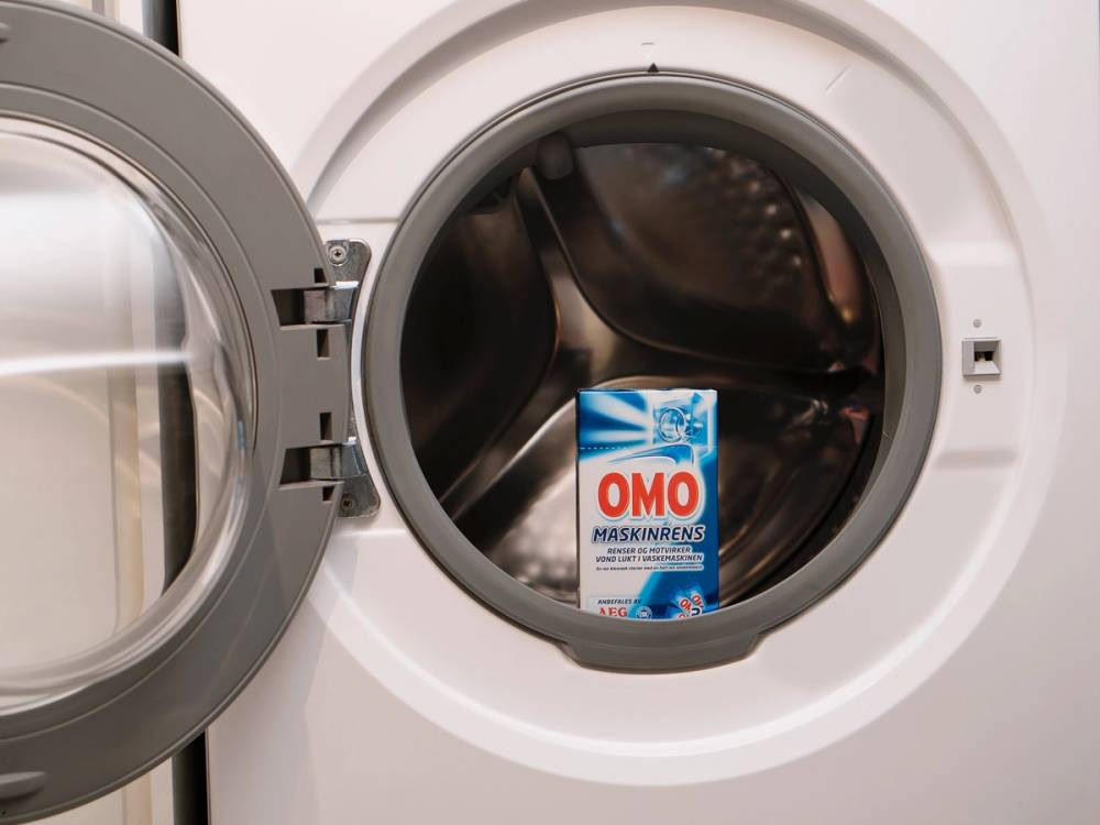 Rensevaskemiddel fra OMO plassert inne i en åpen vaskemaskin, klar for bruk.
