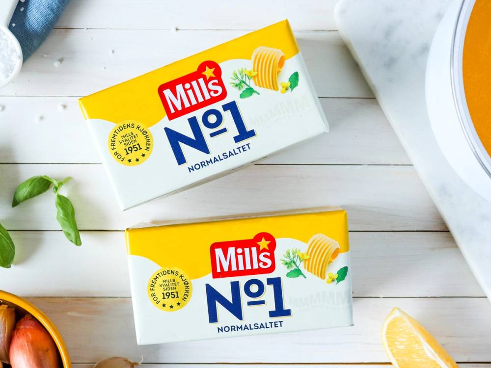 To pakker med Mills No1 smør ligger på et lyst bord med en sitron og noen grønne blader rundt.