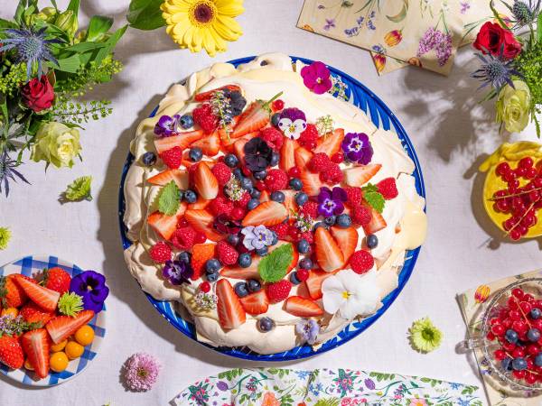 Et fristende dessertbord med ulike frukt og små kaker på et bord dekket med blomster.