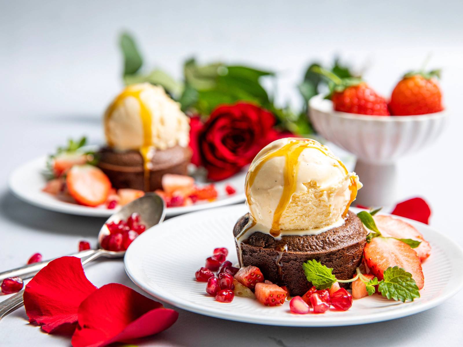En dessert med iskrem, sjokolade, jordbær og en rød rose på en hvit tallerken, egnet for Valentinsdag eller morsdag.