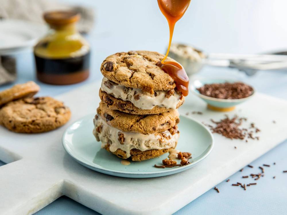 En stabel med fire kjeks med iskrem mellom, med karamellsaus som helles over toppen, på en hvit skjærebrett.
