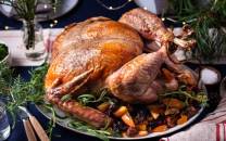 En stekt kalkun på et serveringsfat med grønnsaker og urter rundt, klar til å bli servert.