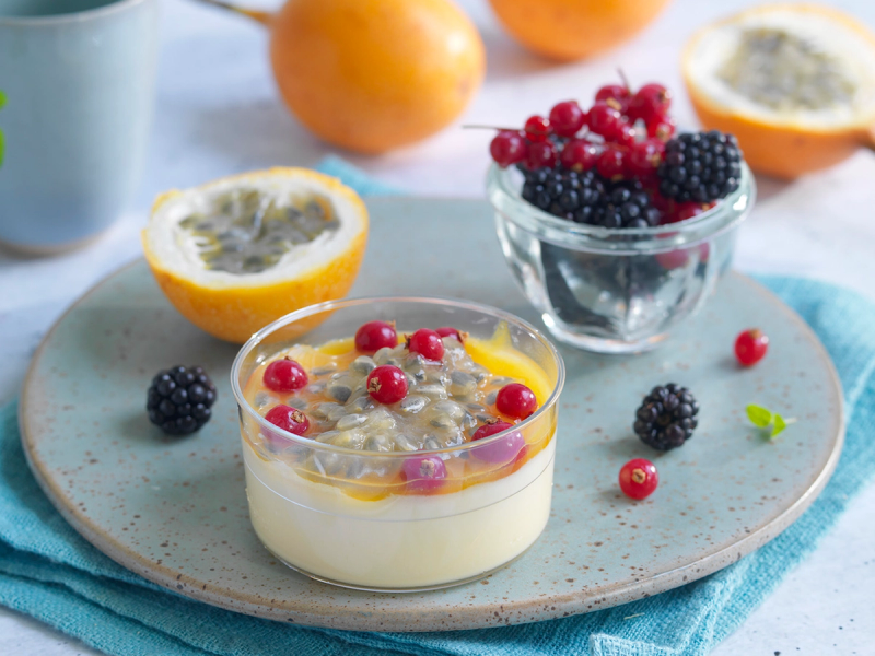 Pasjonsfruktmousse med bær og frukt på en tallerken med hele og halve pasjonsfrukter i bakgrunnen