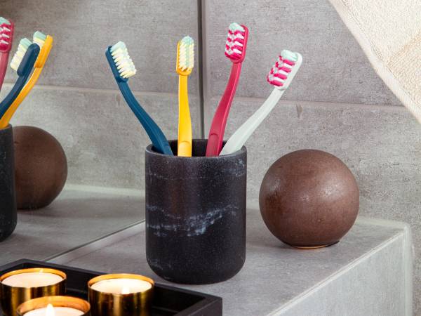 To jordbærfargede og en hvid tannbørste i en svart kopp på et bademøbel, med to runde dekorative steiner ved siden av.
