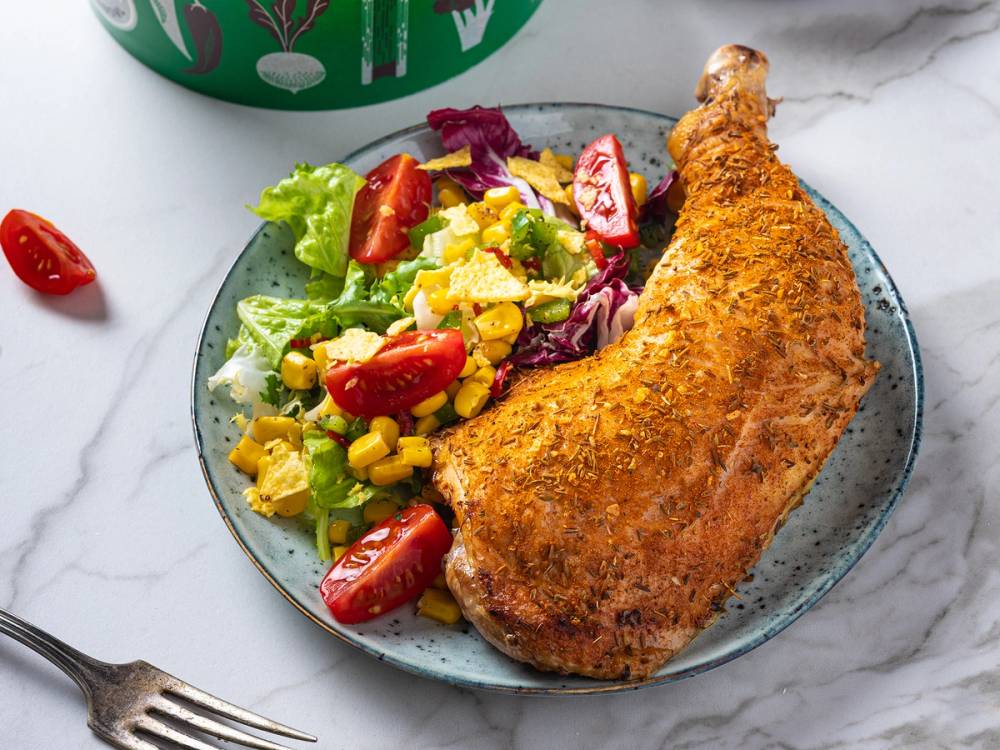 Grillet kyllinglår servert med en frisk salat med cherrytomater og mais på en blå tallerken.