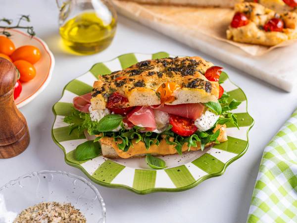 Focaccia med spekeskinke, tomater og fersk basilikum på en grønn og hvit tallerken.