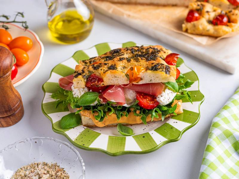 Focaccia med spekeskinke, tomater og fersk basilikum på en grønn og hvit tallerken.