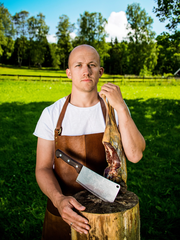 Person med forklær som skjærer i en trestamme utendørs på en grønn eng med trær i bakgrunnen.
