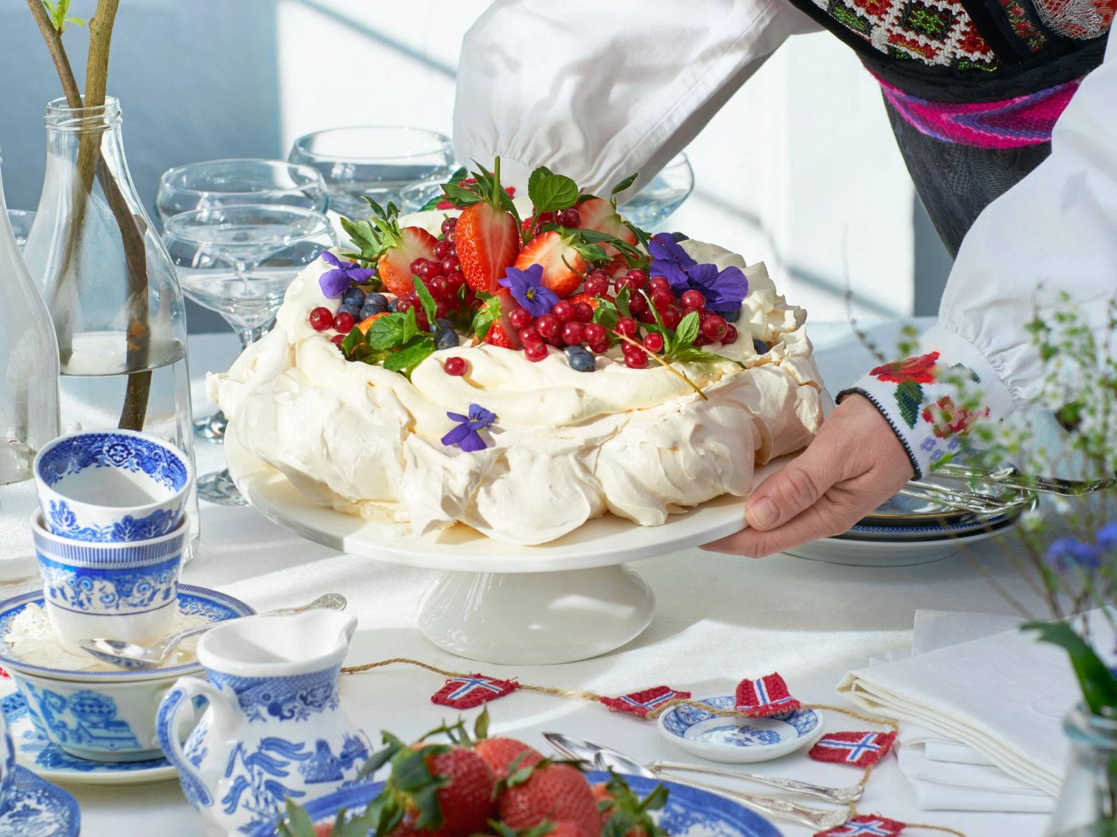 En pavlova med frukt og bær på et festbord under 17. mai-feiring, med norske flagg og tradisjonelt servise rundt.