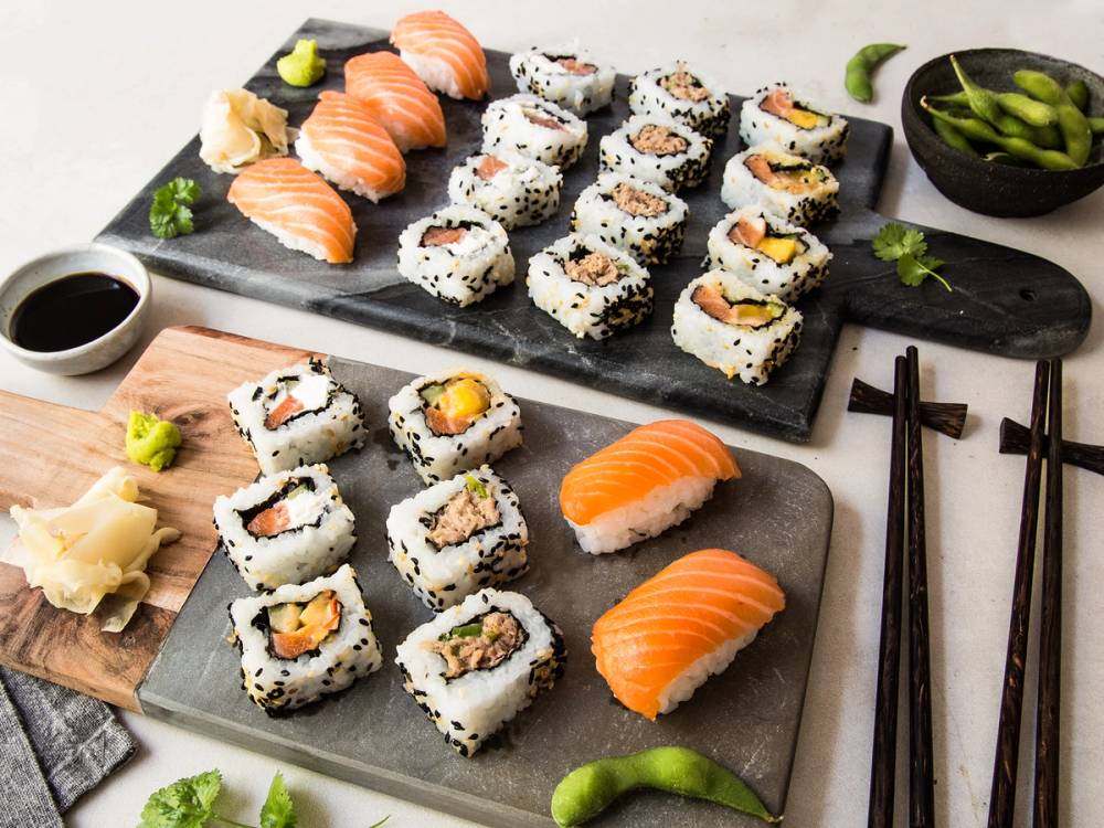 Sushi med 32 biter med laks, kremost og grønnsaker, servert på to serveringsfat med soyasaus og wasabi ved siden av.