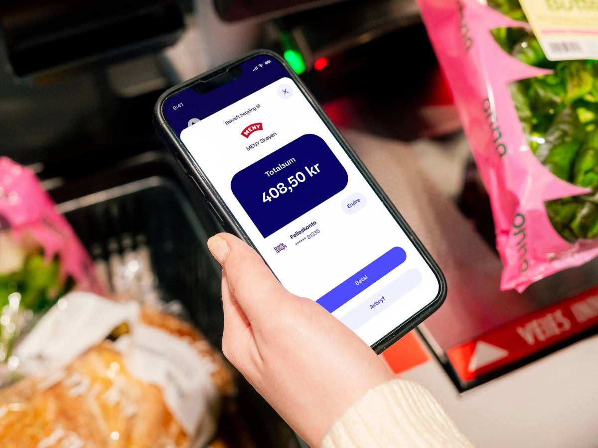 En person holder en smarttelefon som viser Trumf Pay-menyen for 2024 med en saldo på 408,50 kr, omgitt av matvarer i butikkhyllen.