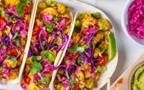 To tacos fylt med blomkål, kål, og grønnsaker, ser ut til å være på et fat med tilbehør i små boller rundt.