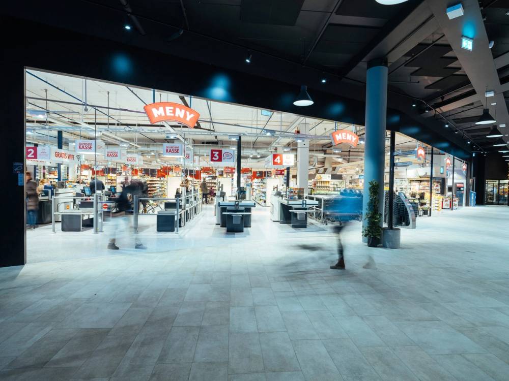 Inngangen til en butikk med kasser og kunder som handler, sett fra utsiden av butikken.