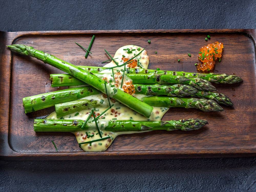 Grønne asparges servert på en treplate med noen små tilbehør og urter, pyntet med sitronskiver.