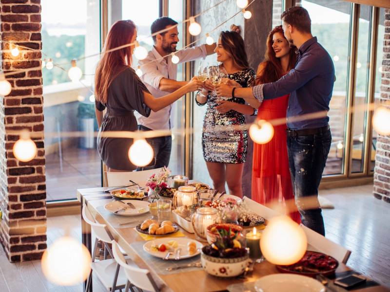 En gruppe mennesker danser og har det gøy rundt et bord med mat og drikke under en nyttårsfest.