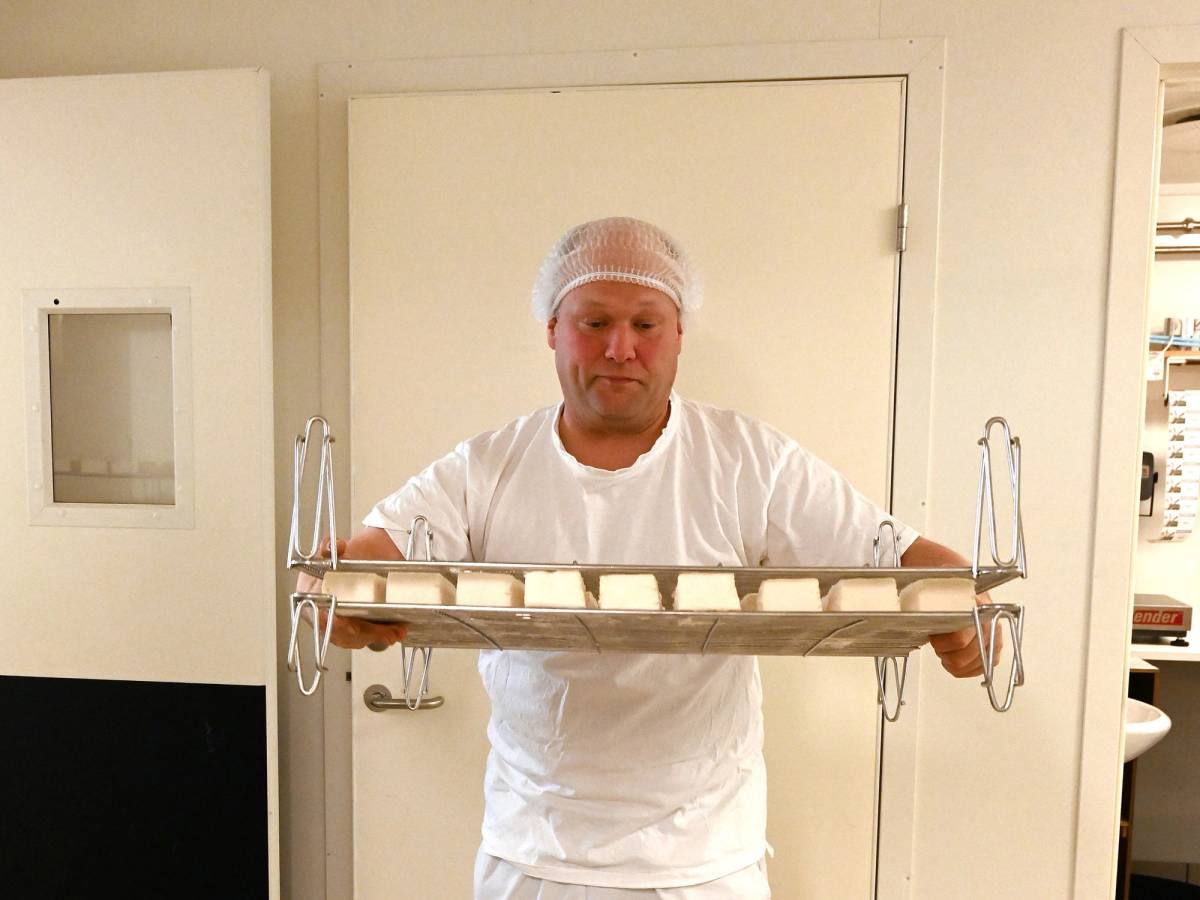 Person holder en stor ost på en tralle i et rom med hvite vegger og dører.